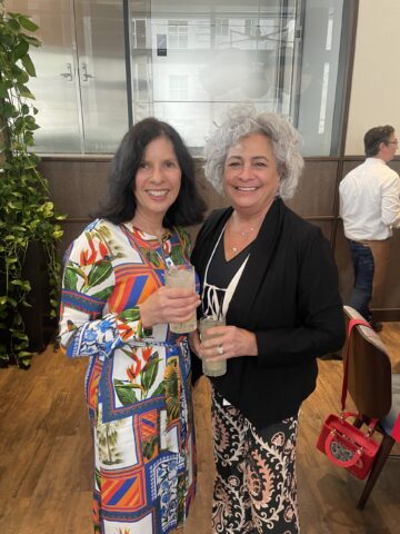 two people standing inside for photo with drinks in hand