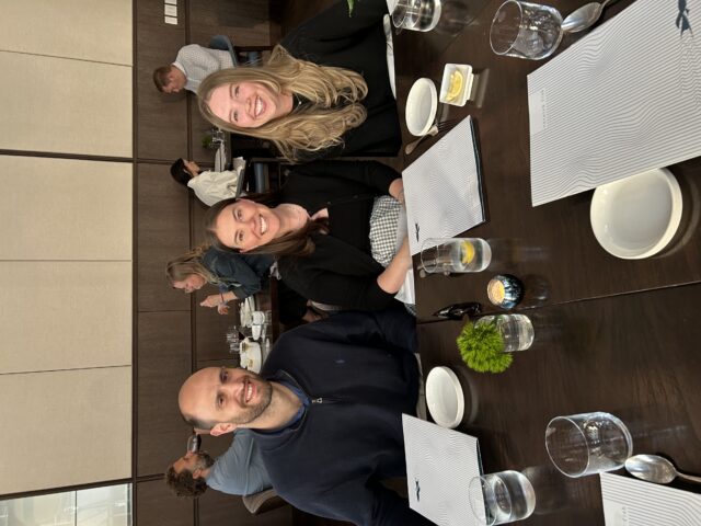 three people sitting at a restaurant table smiling for a photo