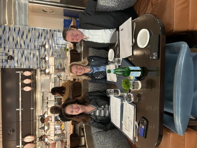 three people sitting at a restaurant table smiling for a photo